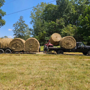 Large round hay bales on a trailer beside a red tractor in a freshly cut field at Retreat at Hope Farm in Springfield, Tennessee.
