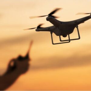 “A person operating a quadcopter drone at sunset, with the drone hovering in the foreground against an orange sky.
