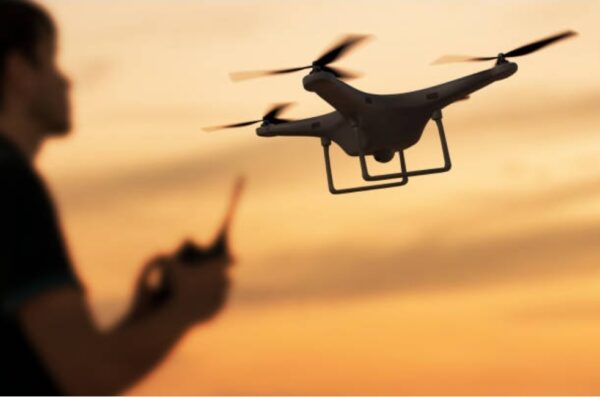 “A person operating a quadcopter drone at sunset, with the drone hovering in the foreground against an orange sky.