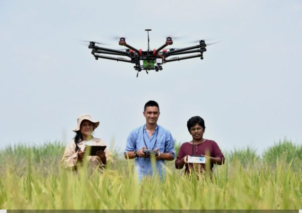 A vibrant group of friends relaxes on the grass while a drone hovers playfully above them, capturing the energy and excitement of flying together. The warm sunlight and open space highlight the joy of shared experiences, making this scene perfect for promoting family memberships, group sessions, and community flying at Hope Farm Flight Club.