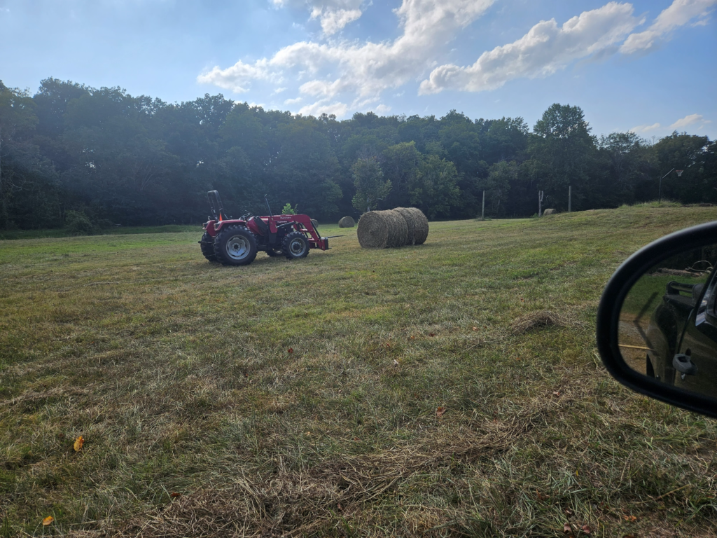 Red tractor beside large round hay bales in a freshly cut field at Retreat at Hope Farm in Springfield, Tennessee.