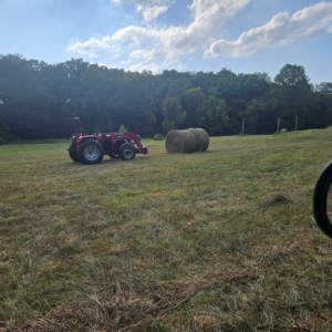 Red tractor beside large round hay bales in a freshly cut field at Retreat at Hope Farm in Springfield, Tennessee.